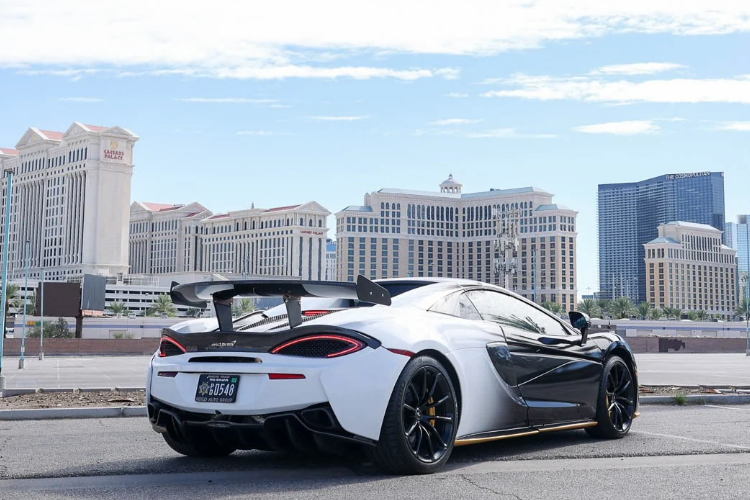 Rear three-quarter view of a wrapped McLaren 570S Spider with custom rear wing overlooking the Las Vegas Strip.