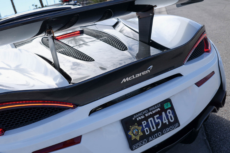 Rear detail of a McLaren 570S Spider featuring the McLaren logo, carbon fiber wing, and custom white wrap.