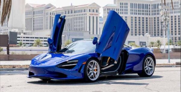 Blue McLaren exotic car rental with butterfly doors up and a backdrop of Las Vegas.