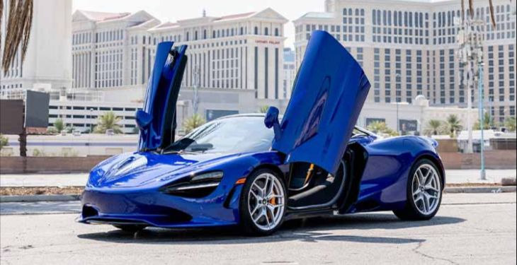 Blue McLaren exotic car rental with butterfly doors up and a backdrop of Las Vegas.