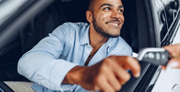 An exotic car renter receiving the key to the exotic car, happy because they have insurance.